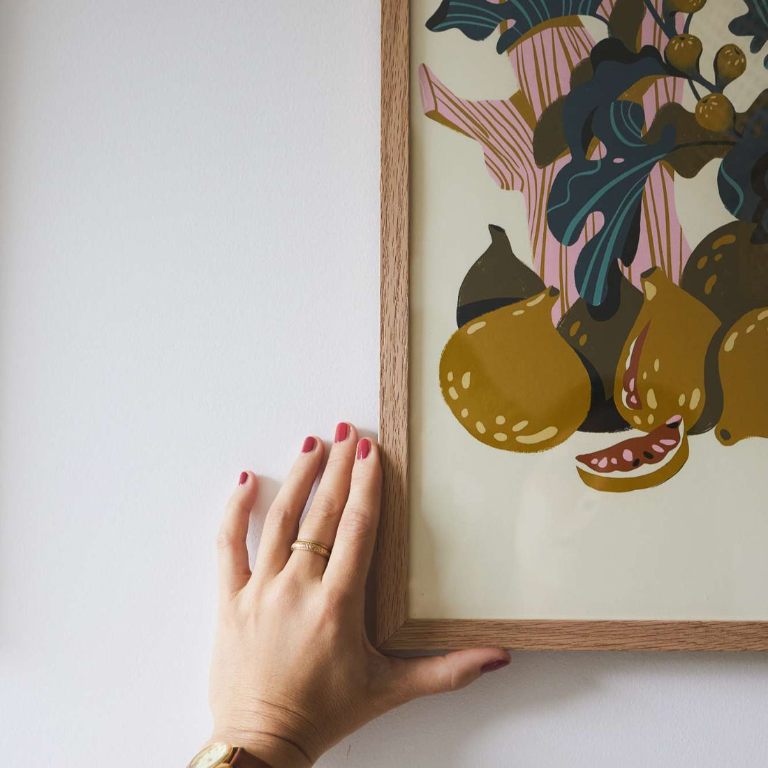 Hand adjusting a framed artwork of fruits on a white wall