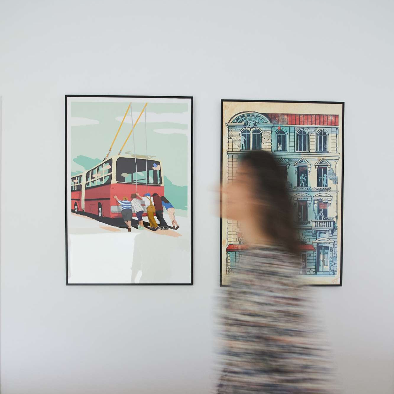 Woman walking past two framed artworks on a wall.